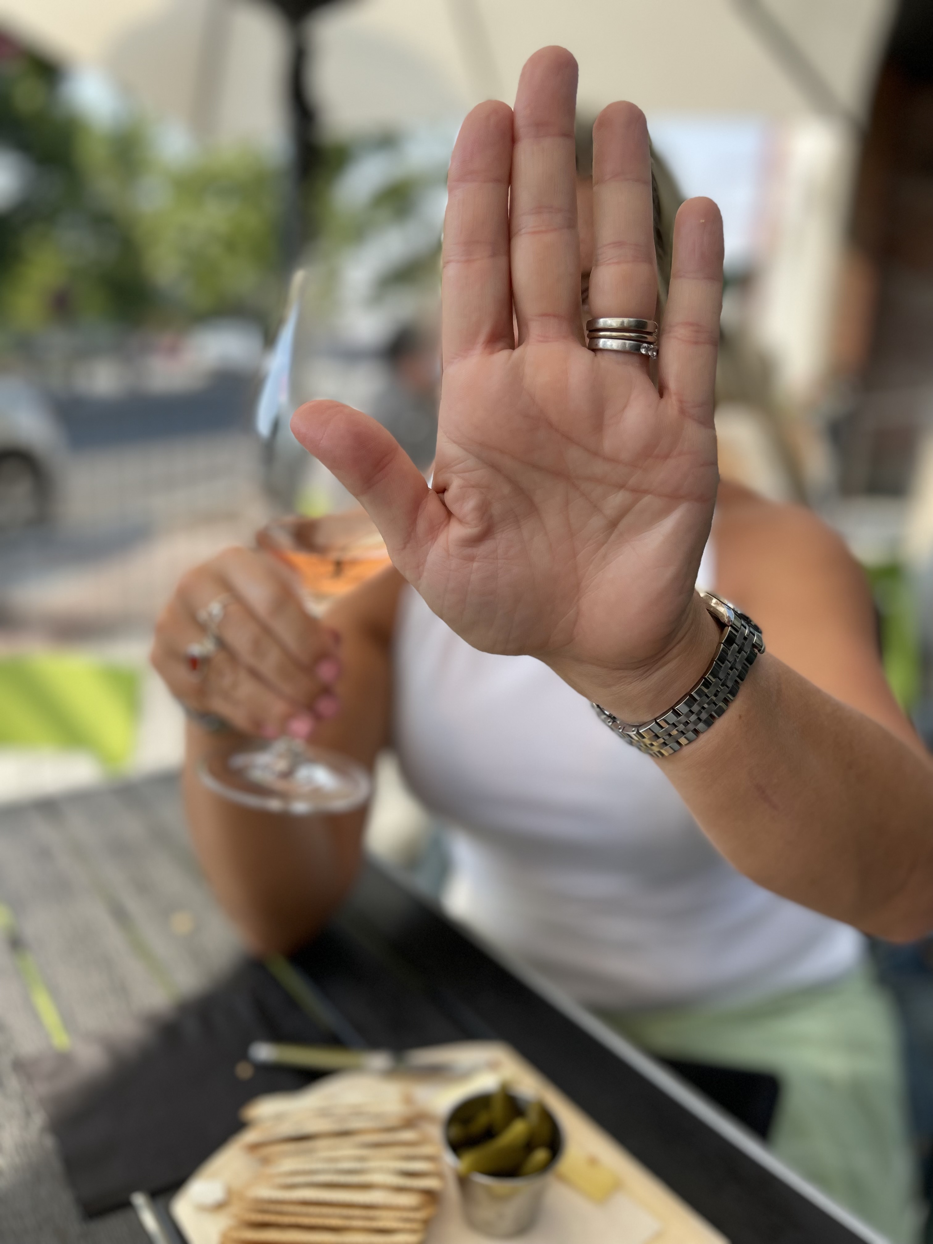 A woman drinking a glass of wine with her hand up as if to stop the camera from seeing her face.
