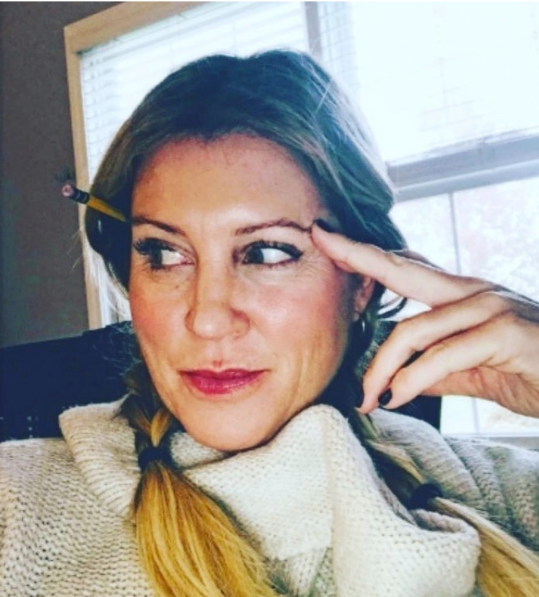 Blon woman with braids looking to the side, smiling, with a pencil behind her ear.