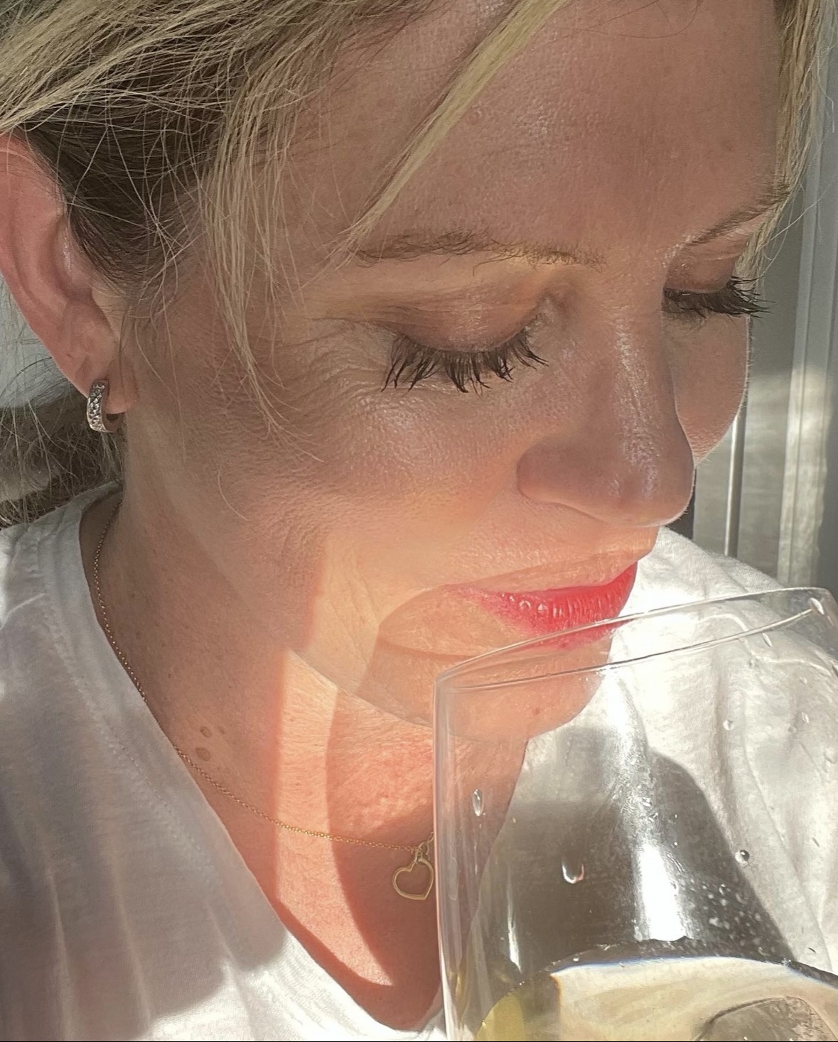 Close up of a blond woman drinking chardonnay with long eyelashes.