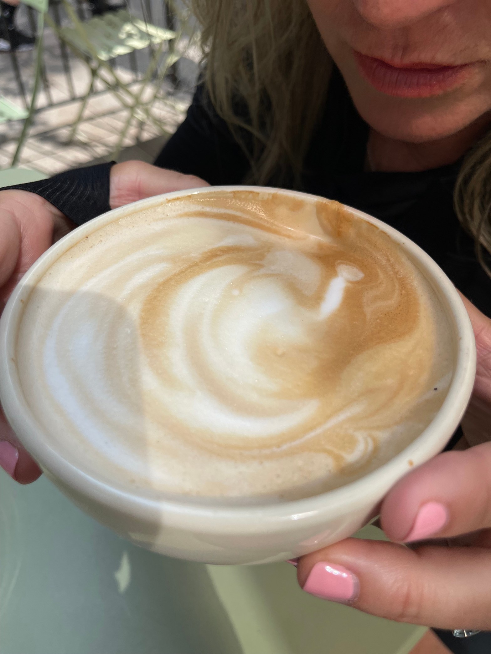 Close up of a woman holding a cappuccino in her hands about to drink it.