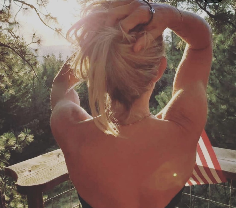 Blond woman from the back looking out at the sunrise from a balcony.