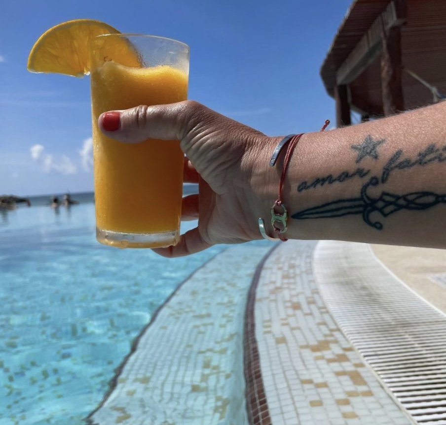 A woman's arm stretched out over a pool with a tattoo that reads Amor Fati.